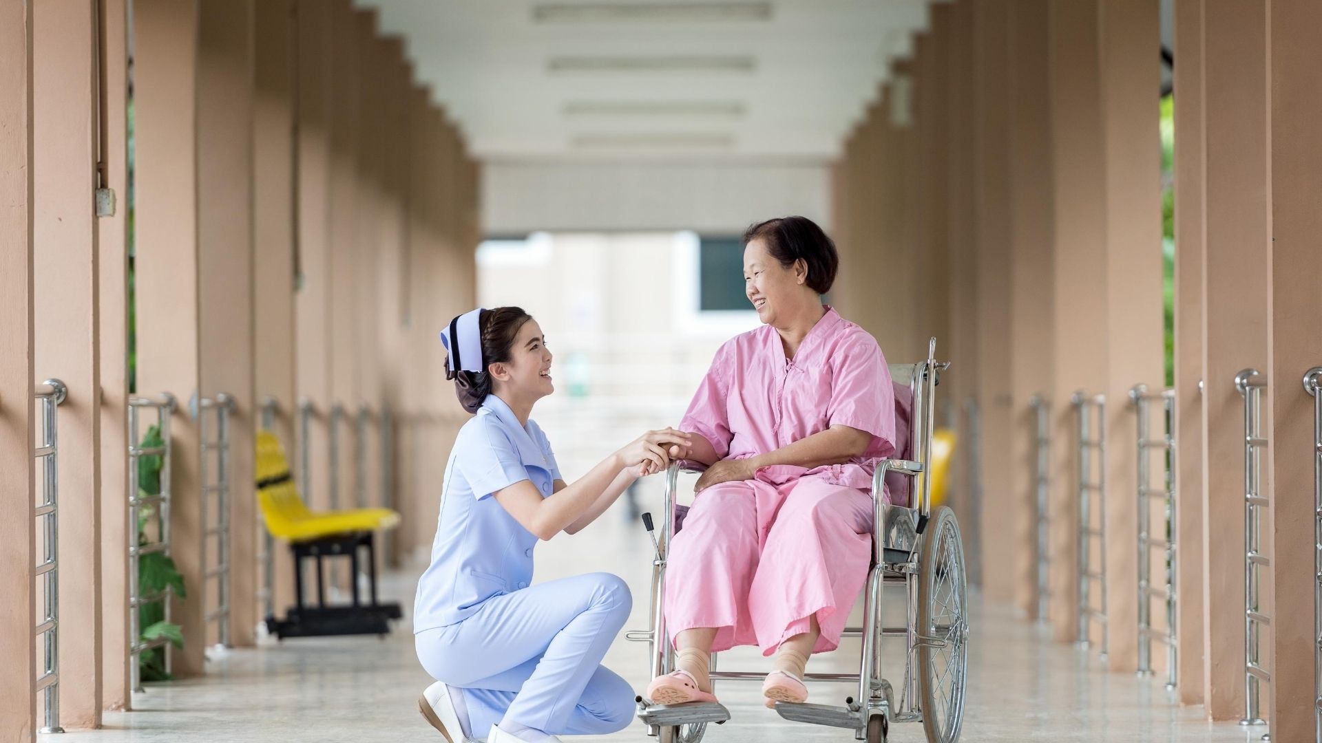 Asian woman in wheelchair smiling, nurse standing by her side in hospital