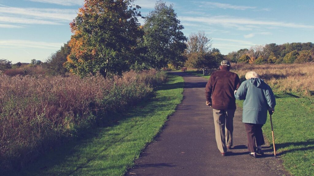 Elderly man and woman walking hand in hand on an empty road in the countryside