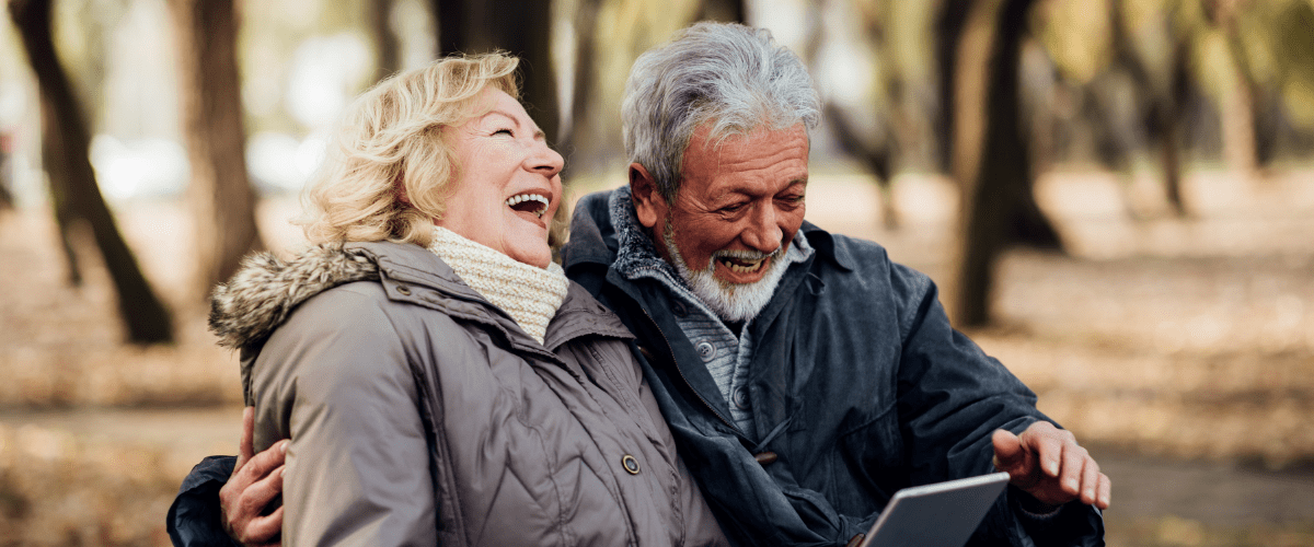 Older man and woman sitting on a park bench laughing